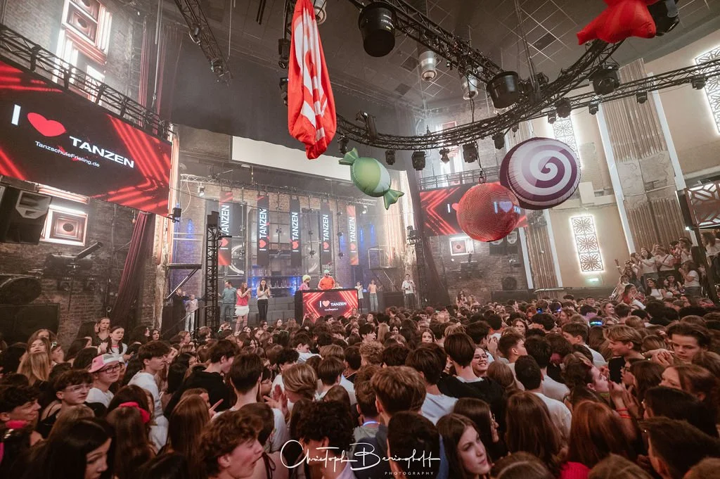 A large concert featuring a dancing crowd, a stage with musicians, large candy decorations, and LED displays reading 'I ❤️ DANCING' at an indoor venue.