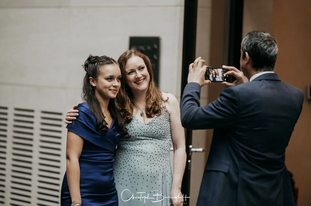 Drei Menschen, zwei Frauen und ein Mann, beim Anfertigen eines Fotos in einem Innenraum.