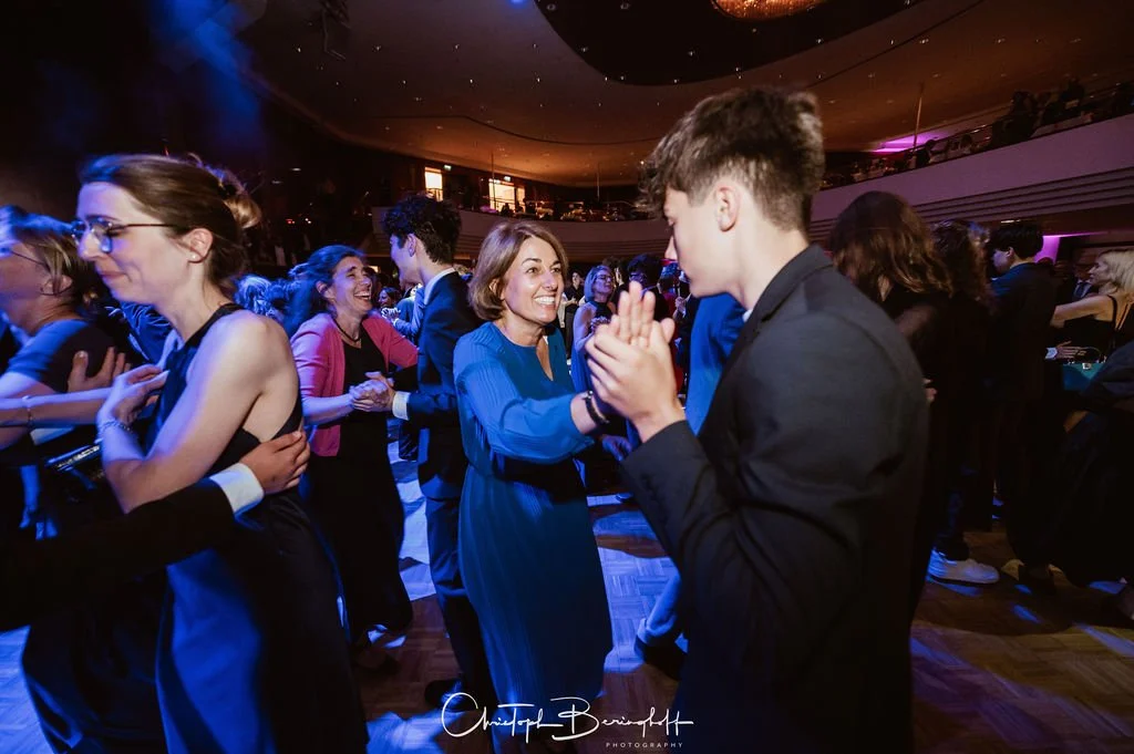 Menschen tanzen und lachen auf einer Party in einem festlich beleuchteten Saal.