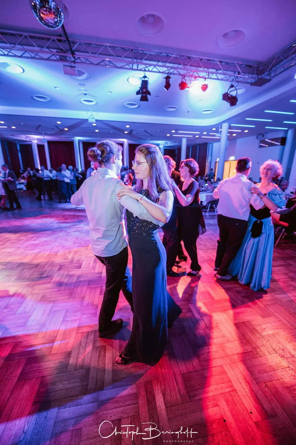 Menschen tanzen auf einem festlichen Ballsaal mit bunten Lichtern.