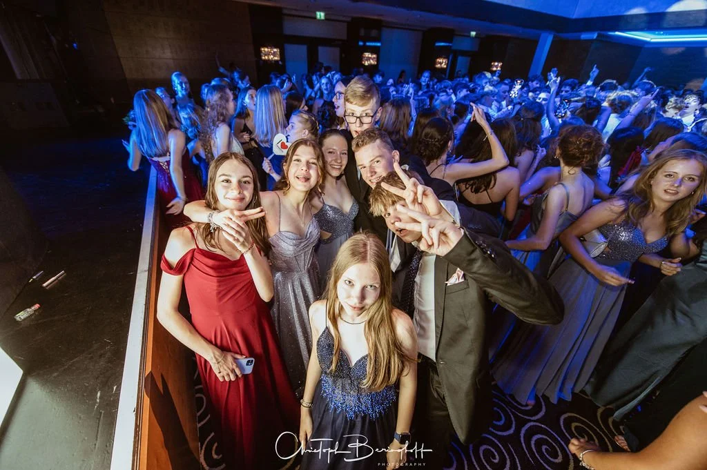 Junge Menschen feiern auf einer Tanzveranstaltung in eleganten Kleidern. Die Stimmung ist fröhlich und lebendig.