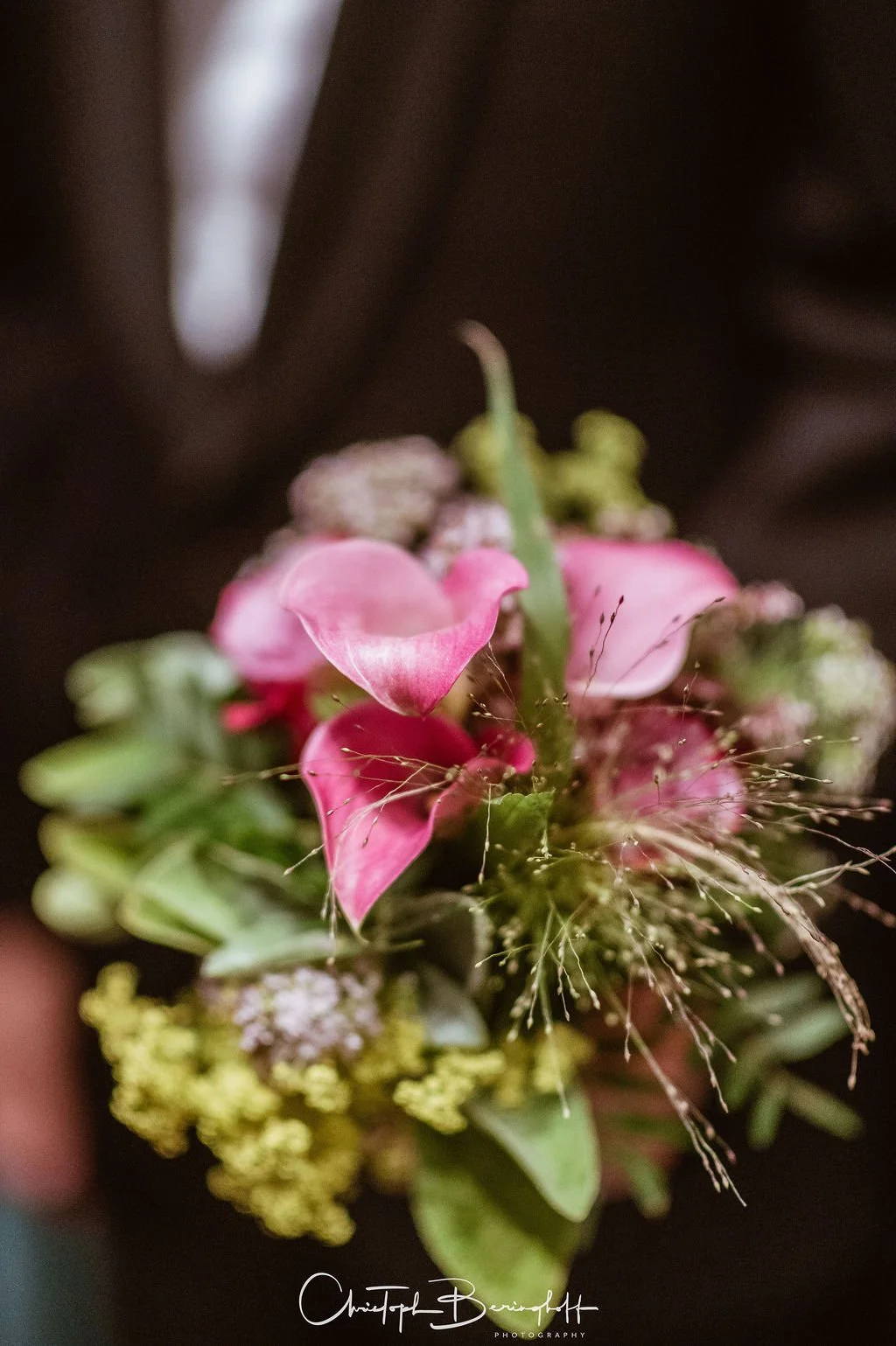 Nahaufnahme eines Blumenstraußes mit pinken und grünen Blüten auf dunklem Hintergrund.