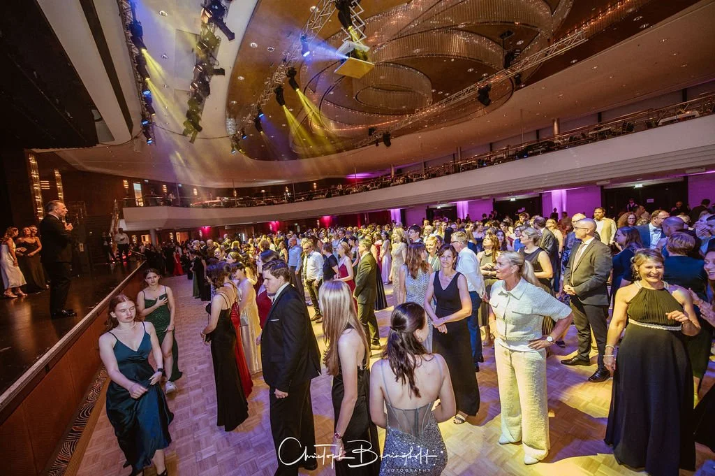 Menschen tanzen und feiern in einem festlich beleuchteten großen Ballsaal bei einer Gala oder Party.