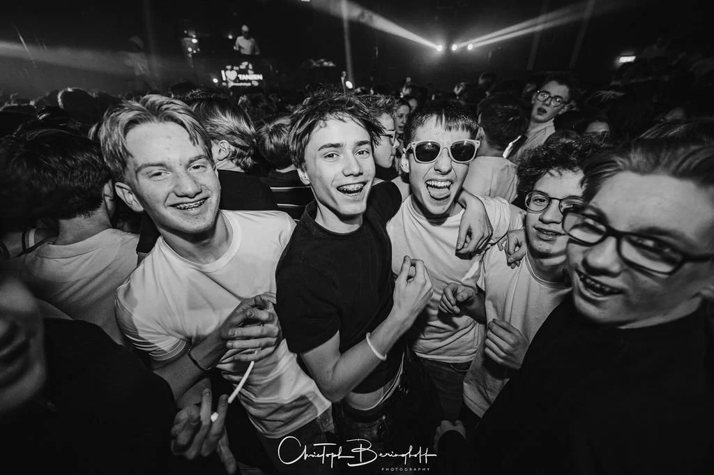 A group of young people having fun at a party or concert, smiling and cheering.