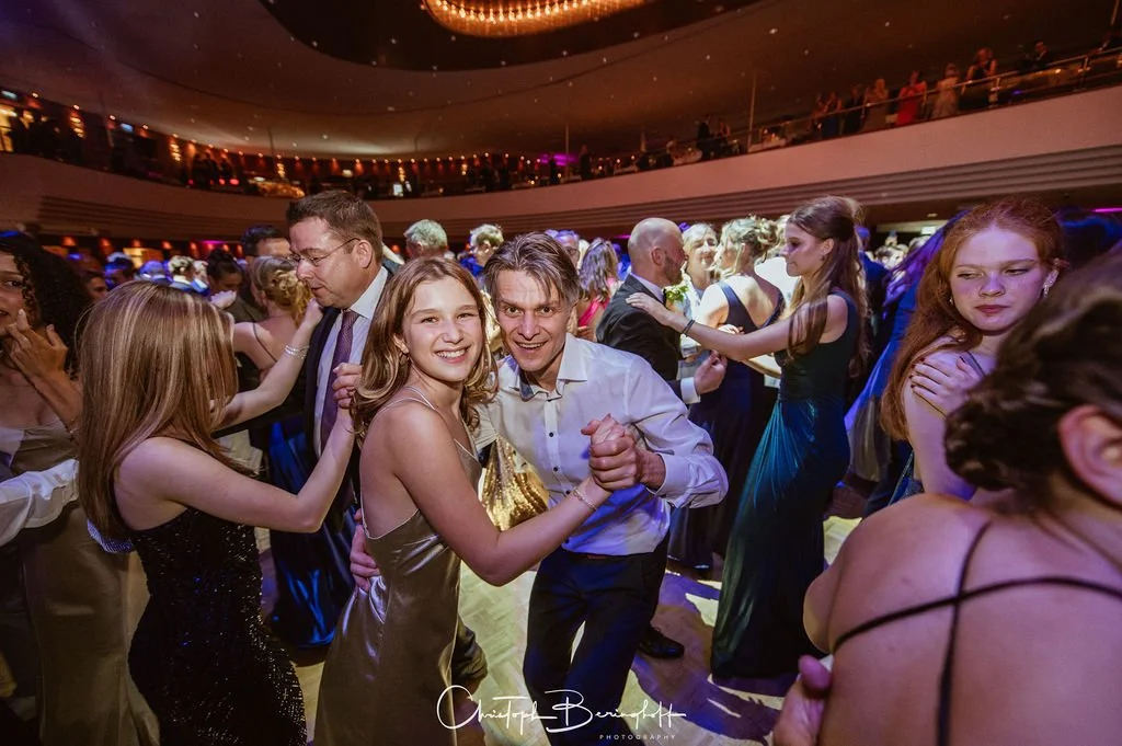 Menschen tanzen bei einer Veranstaltung im festlichen Rahmen, einige lachen und haben Spaß, im Hintergrund sind weitere Gäste zu sehen.