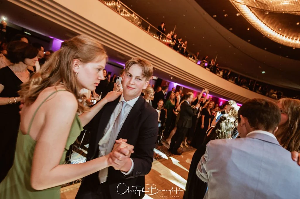 Tanzende Menschen auf einer Gala im eleganten Veranstaltungsraum mit mehrstöckigem Design und buntem Beleuchtungsambiente.