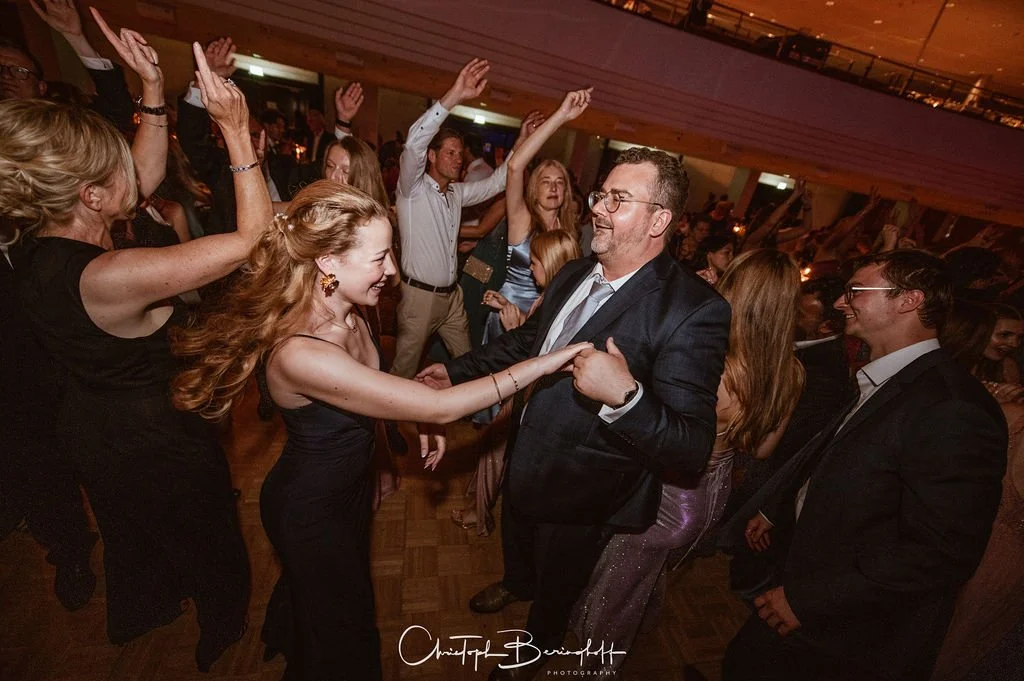 Menschen tanzen und lachen auf einer Party, es wird gefeiert, die Atmosphäre ist lebhaft und fröhlich.