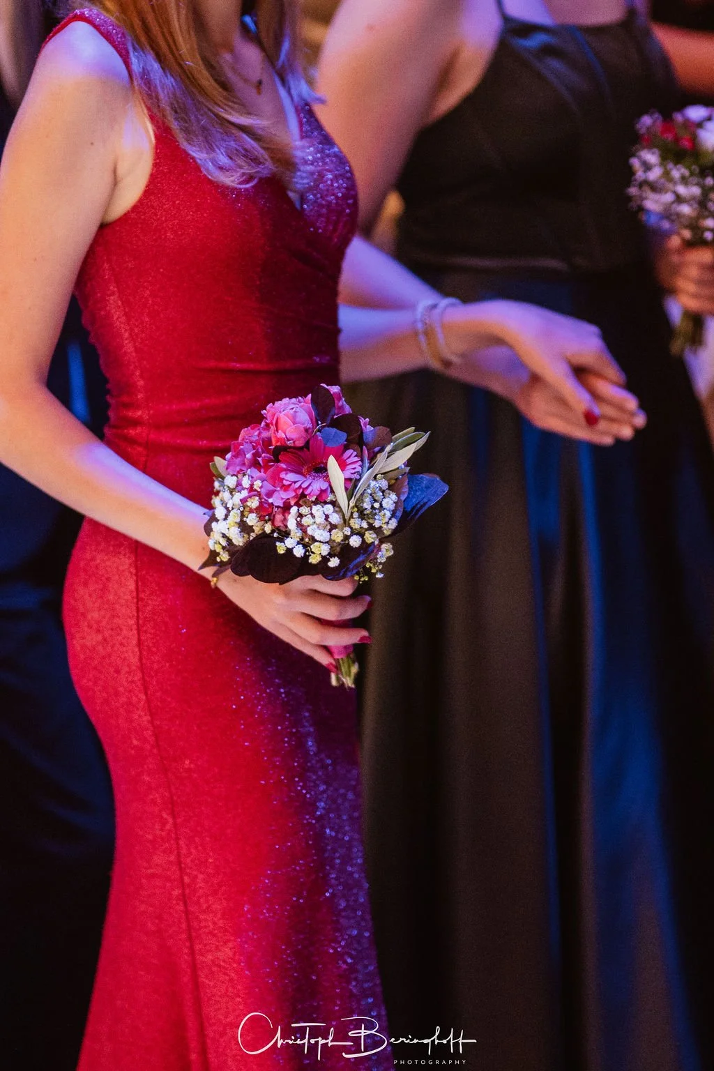 Frau in rotem Abendkleid hält einen Blumenstrauß bei einer Feier