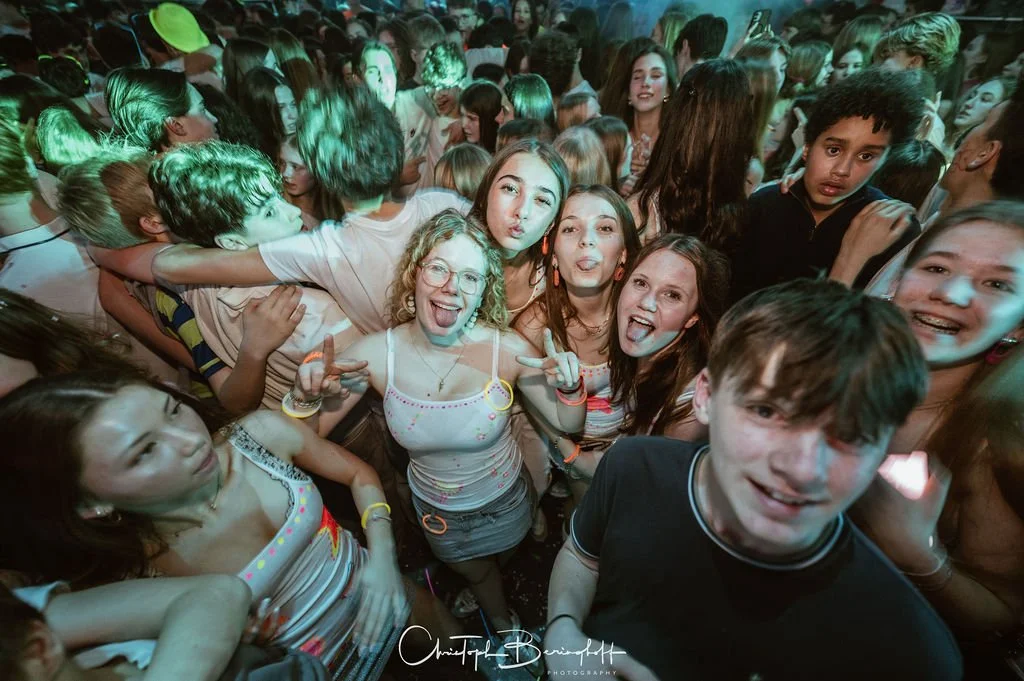 People are dancing and celebrating at a party in a dark, colorful setting.