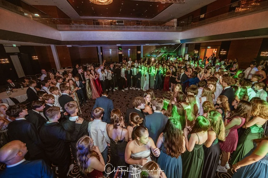 Bälle und Tanzveranstaltung in einem großen, eleganten Ballsaal mit vielen jungen Menschen in formeller Kleidung, die tanzen und feiern.