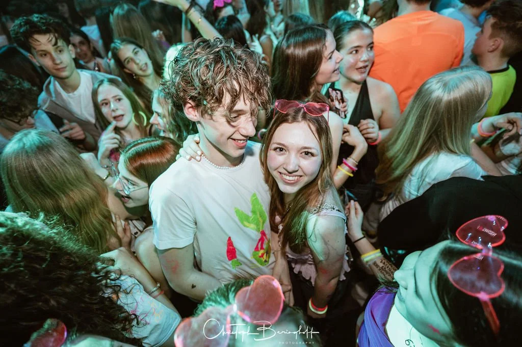Young girls and young women at a party, surrounded by lots of people, laughing and celebrating.