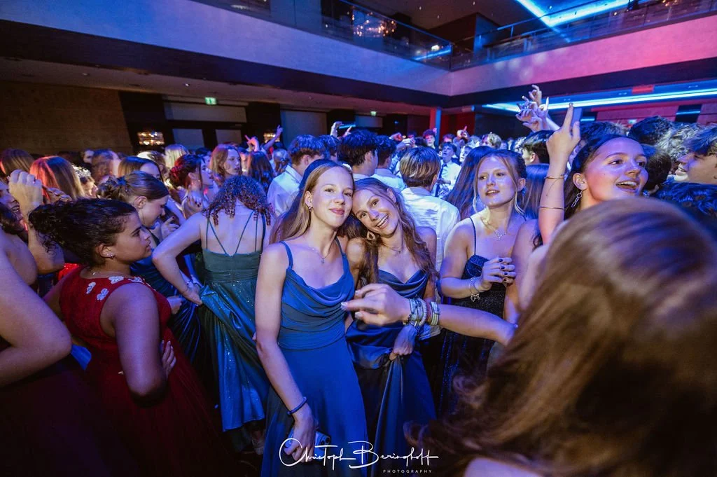 Menschen tanzen und feiern auf einer Party in einem dunklen, modernen Raum mit blauen und roten Lichtern.