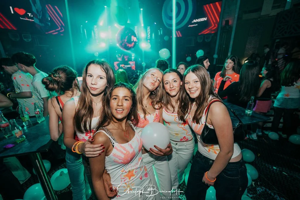 A group of young women is posing in the party room, surrounded by colorful lights and balloons.
