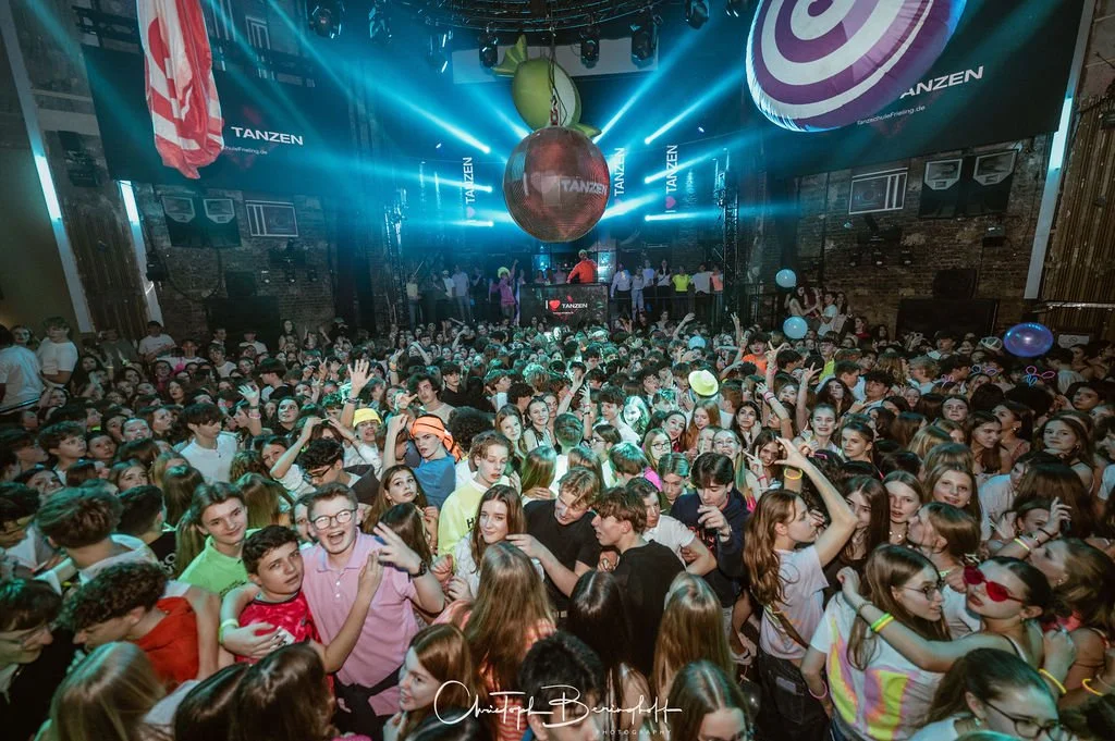 Many teenagers are dancing at a party in a disco with colorful lights and balloons.