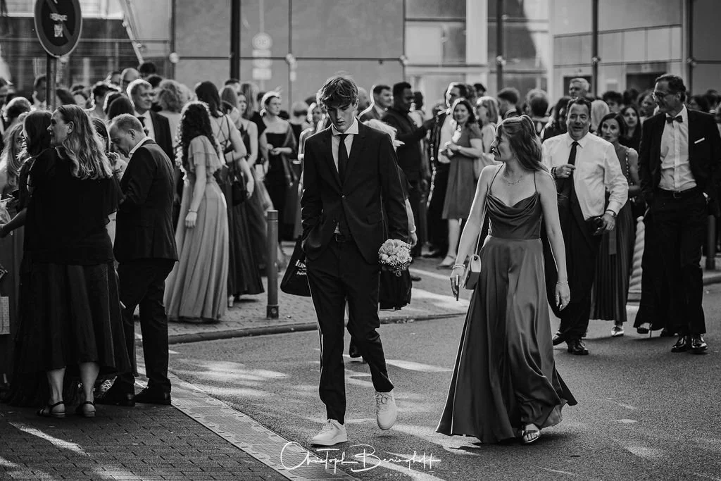 Menschen in formeller Kleidung bei einer Event- oder Hochzeitfeier auf einer Stadtstraße in Schwarz-Weiß.
