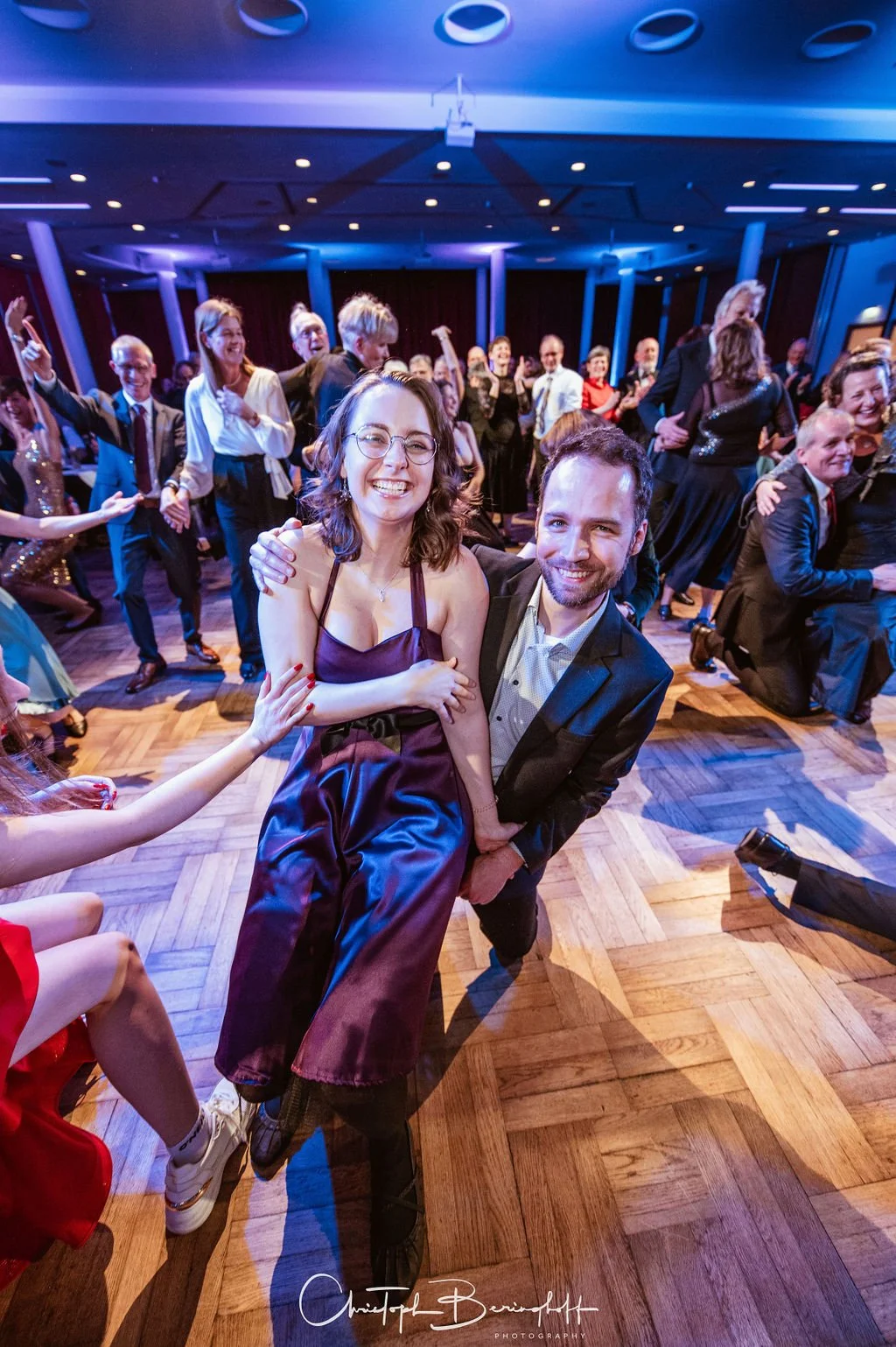 Menschen tanzen und lachen auf einer festlichen Party im festlich beleuchteten Raum.