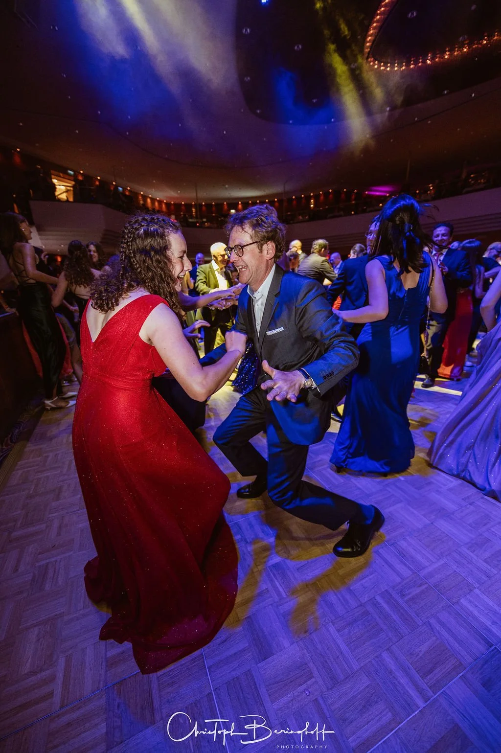 Menschen tanzen auf einer Party, die in einem eleganten Saal mit buntem Licht und voller Stimmung ist.