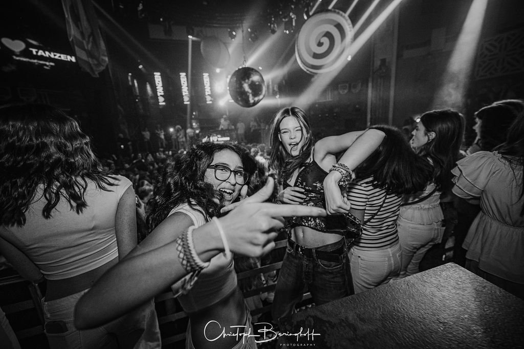 Women are dancing and partying in a nightclub; there are lots of lights, a disco ball, and a spiral-shaped light display.