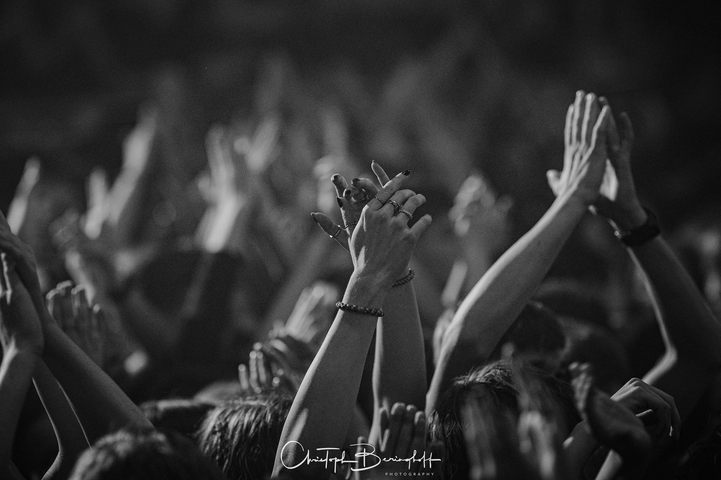 Menschen bei einem Konzert oder einer Feier, einige Hände und Arme in die Luft gestreckt, im Schwarz-Weiß-Stil