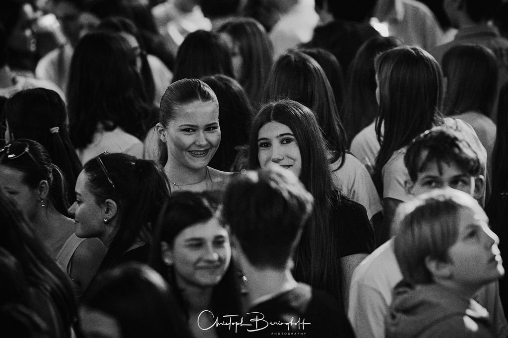 A group of young people at a gathering or event; many are smiling and chatting; black-and-white photograph