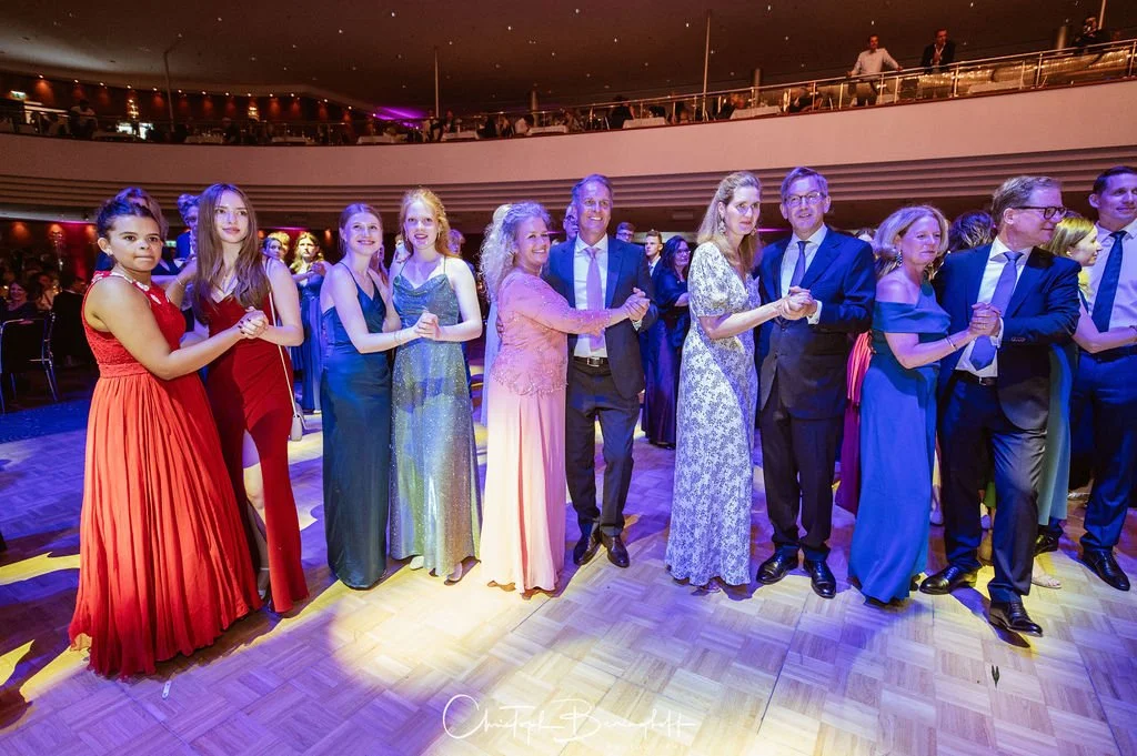 Menschen tanzen Arm in Arm auf einer Hochzeitsfeier im festlichen Abendkleid