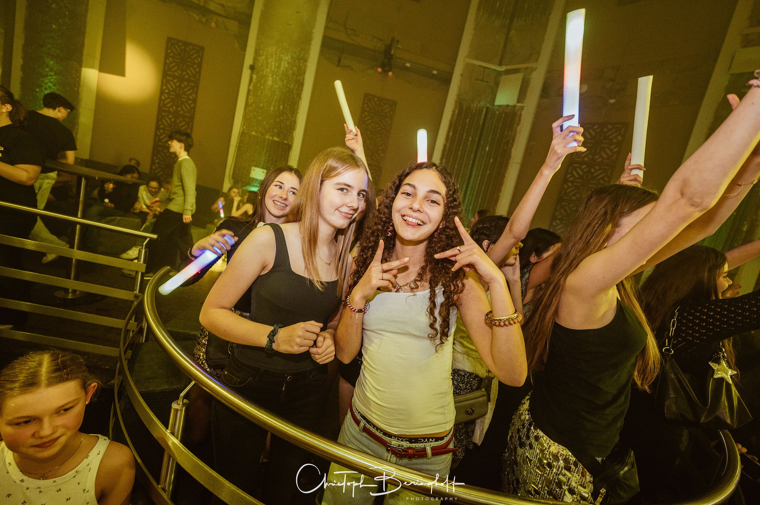 Gruppe junger Frauen, die bei einer Party mit Lichtstäben tanzen und lächeln.