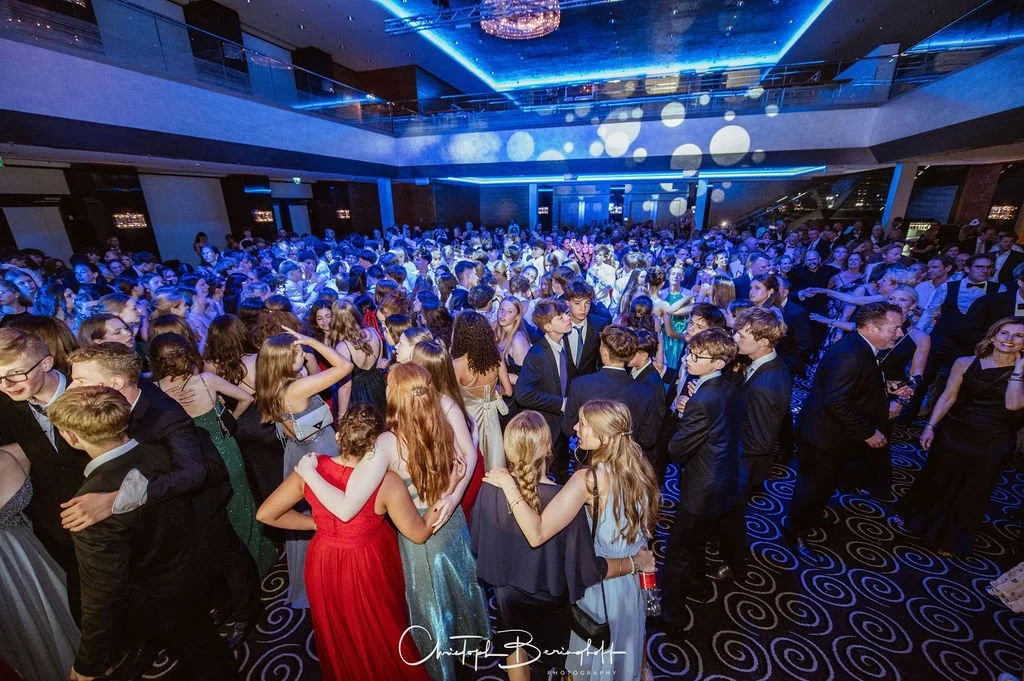 Menschenmenge auf einer Party, viele junge Leute in formeller Kleidung, im Hintergrund blaue Lichter und dezentes Beleuchtungsspektakel