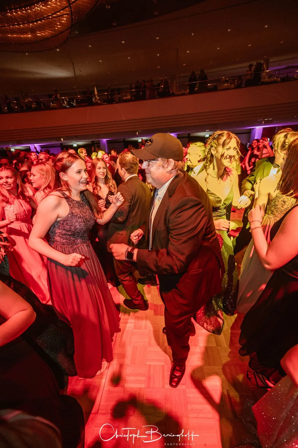 Menschen tanzen auf einer Party im festlichen Abendkleid und Anzügen, während sie fröhlich lachen und feiern.