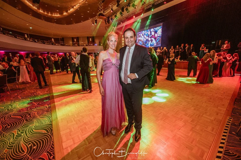 Ein Tanzparkett mit tanzenden Paaren und einem großen Bildschirm im Hintergrund, festliche Atmosphäre bei einer Gala oder Ball, mit bunten Lichtprojektionen und Gästen in eleganter Kleidung.