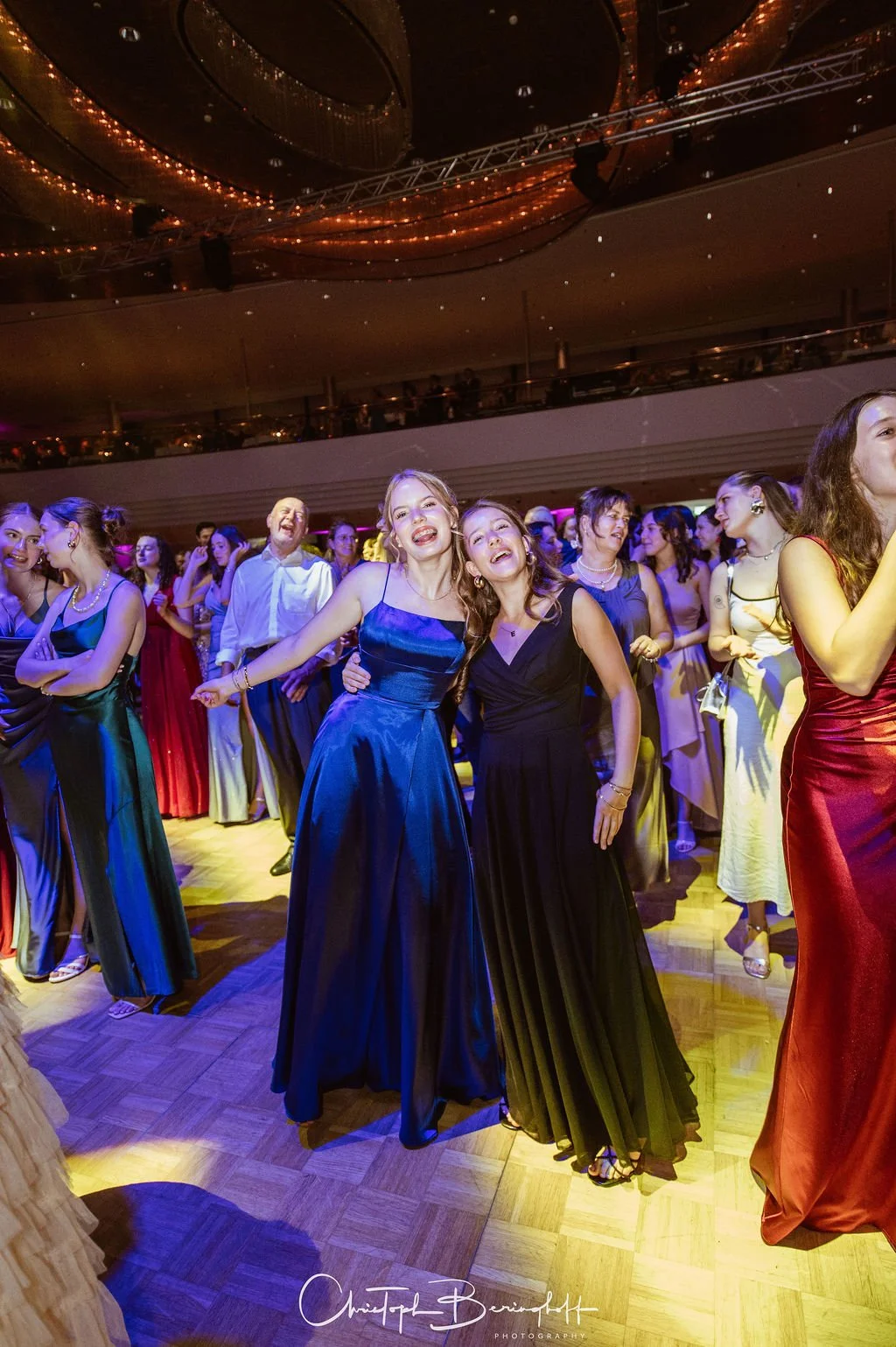 Junge Frauen in eleganten Abendkleidern tanzen und lachen auf einem festlichen Ballsaal