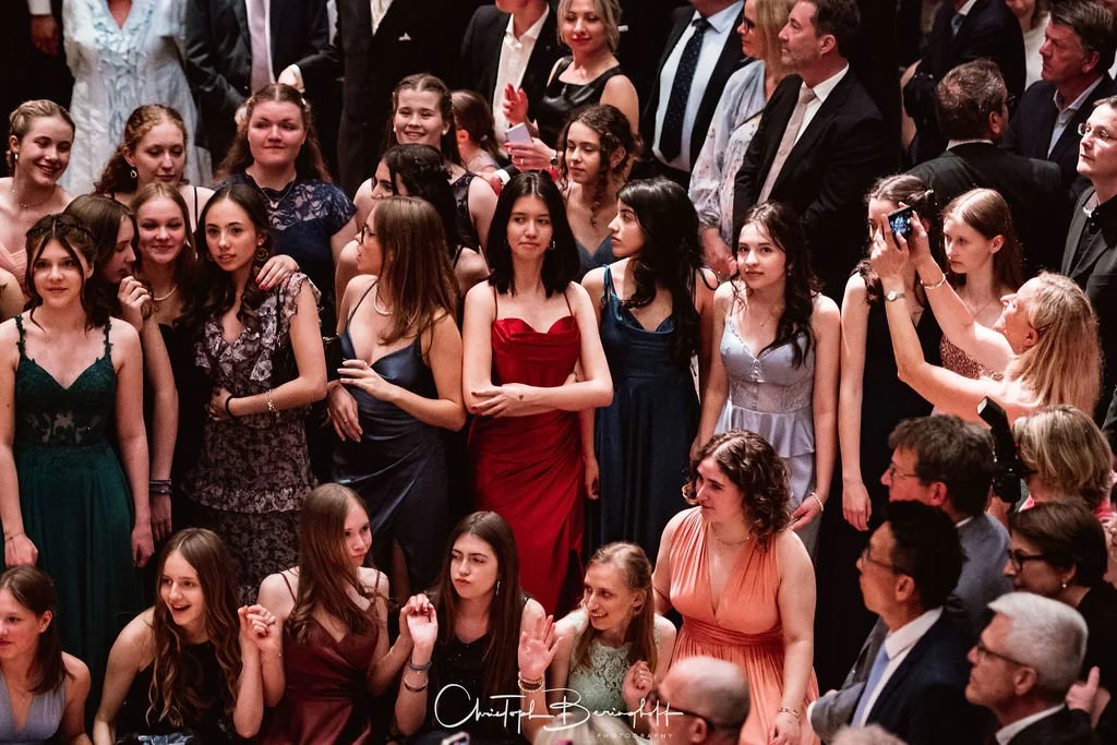 Junge Frauen in formeller Kleidung bei einer Veranstaltung, einige machen Fotos, in einer Gruppe.