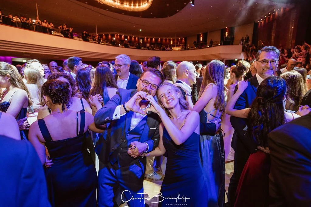 Menschen tanzen und feiern in eleganter Kleidung auf einem festlichen Event in einem Veranstaltungsraum.