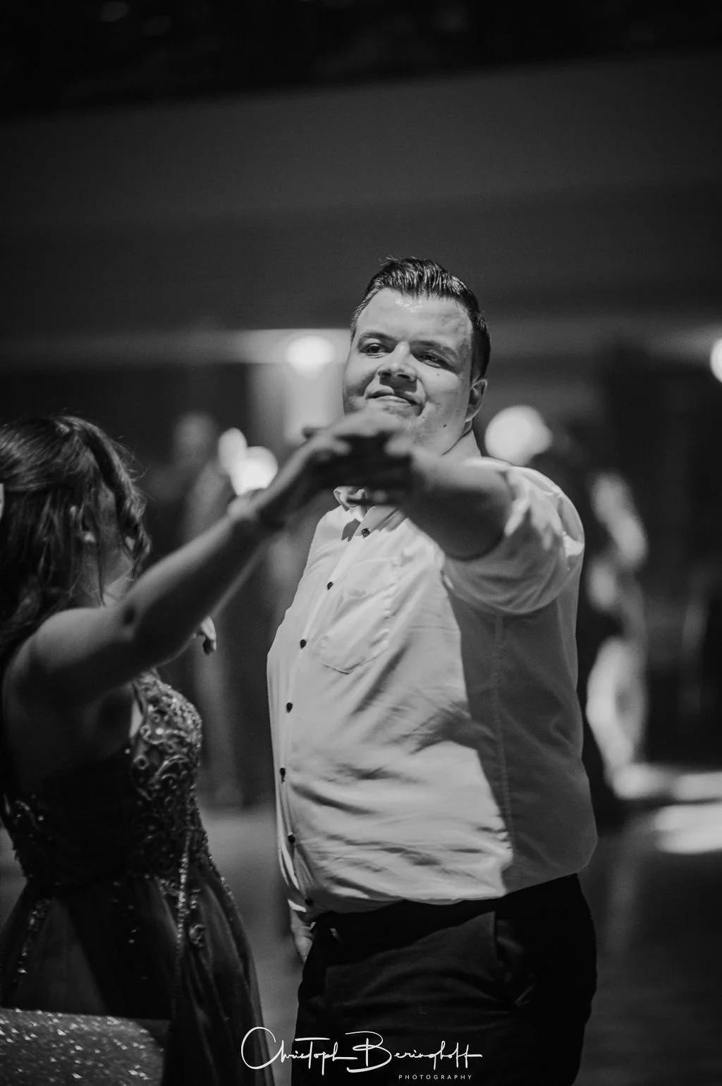 Ein Mann und eine Frau tanzen auf einer Party, die Szene ist schwarz-weiß, im Hintergrund sind andere Feiernde sichtbar.