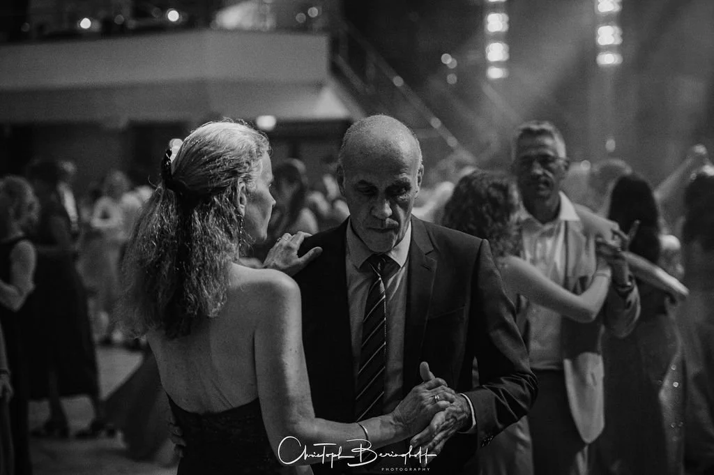 Menschen tanzen auf einer Party, Schwarz-Weiß-Foto, im Hintergrund andere Tanzpaare, eine elegante Atmosphäre.