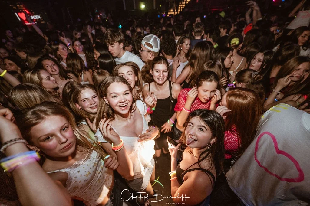 Young people are dancing and partying at a party with neon lights in the background.