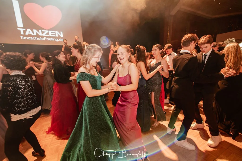 Junge Erwachsene tanzen und lachen auf einer Tanzveranstaltung in eleganten Kleidern und Anzügen, im Hintergrund ein Bildschirm mit dem Text "Ich liebe Tanzen" und einer Internetadresse.
