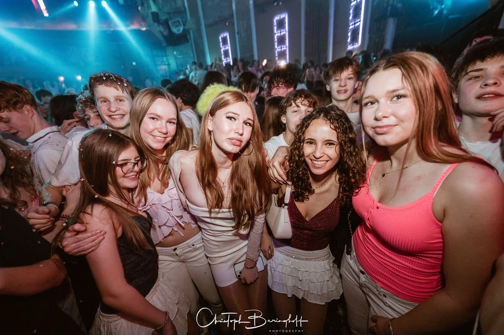 A group of young people partying in a dark disco with colorful lights.