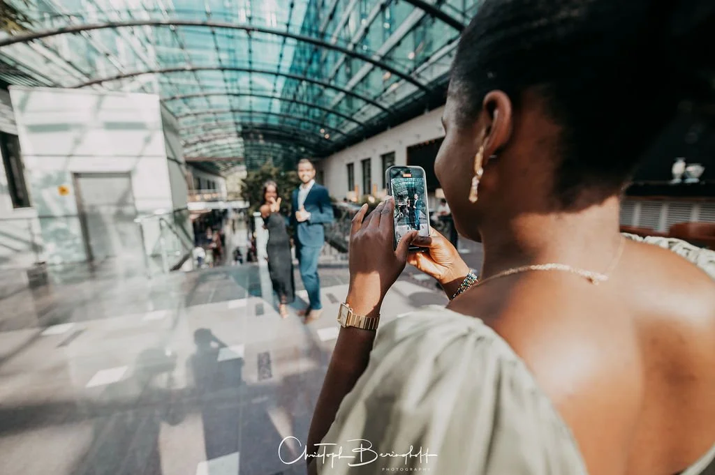 Eine Frau fotografiert ein Paar, das sich in einem modernen, lichtdurchfluteten Gebäude befindet.