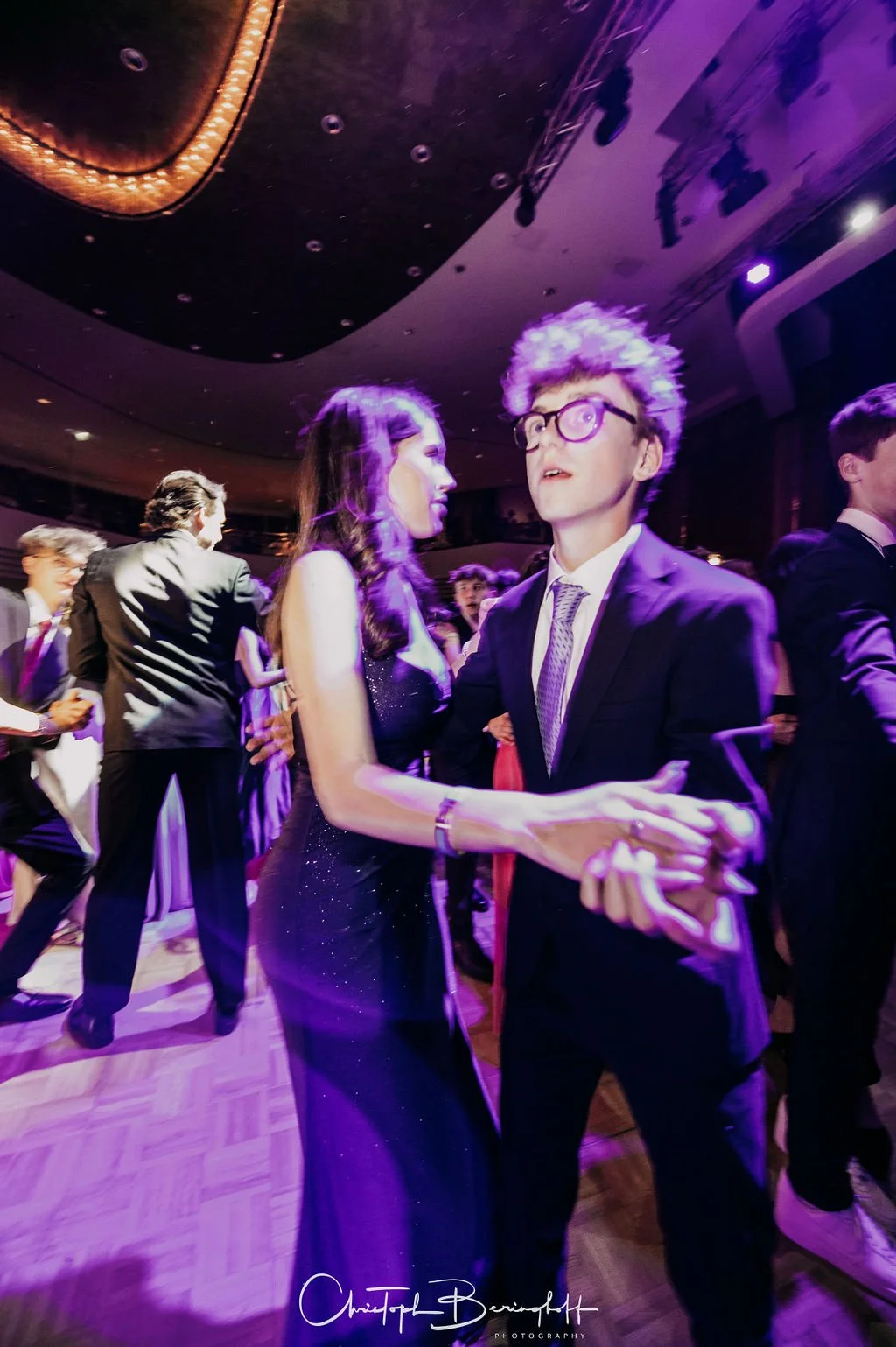 Menschen tanzen auf einer Party im eleganten Schwarz-Weiß-Look, mit einem Mann mit grauen, lockigen Haaren und Brille im Vordergrund.
