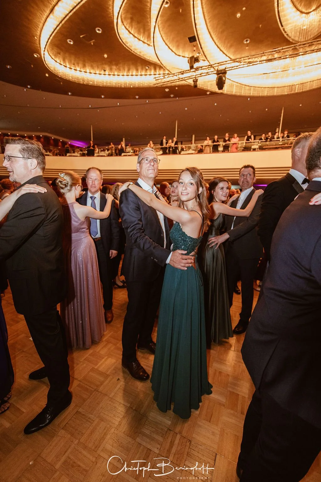 Nach einem formellen Ball tanzen Menschen im eleganten Kleid und Anzug auf der Tanzfläche im Saal, der mit warmem Licht beleuchtet ist.