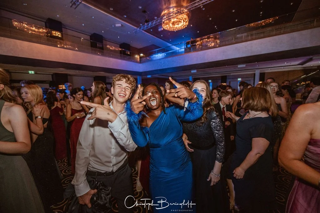 Menschen feiern in einem festlich dekorierten Saal bei einer Party, einige lachen und posieren für die Kamera.