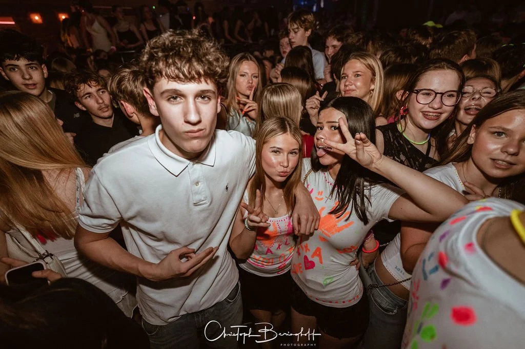 A group of young people at a party, taking photos and having fun in a dimly lit setting with lighting effects.