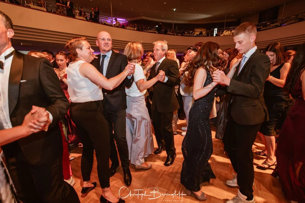 Menschen tanzen in eleganter Kleidung bei einer Hochzeit oder Gala in einem festlichen Veranstaltungsraum.