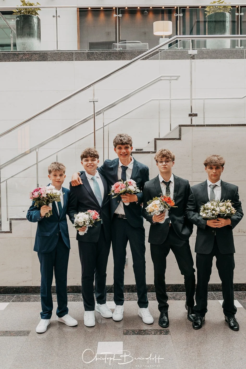 Fünf Jungen in Anzügen, die Blumen halten, bei einer formellen Veranstaltung
