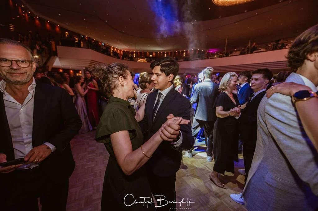 Menschen tanzen und unterhalten sich bei einer eleganten Party in einem festlich dekorierten Saal.