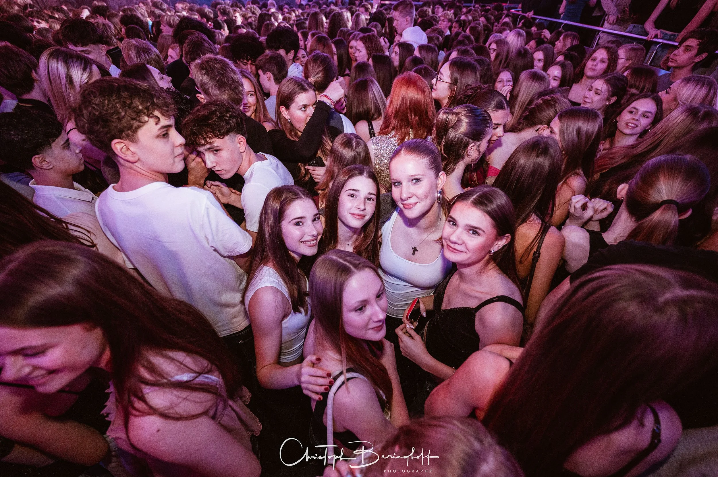 Gruppe junger Menschen bei einer Party, die eng beieinander stehen und lachen, mit einigen, die in der Mitte des Bildes posieren.