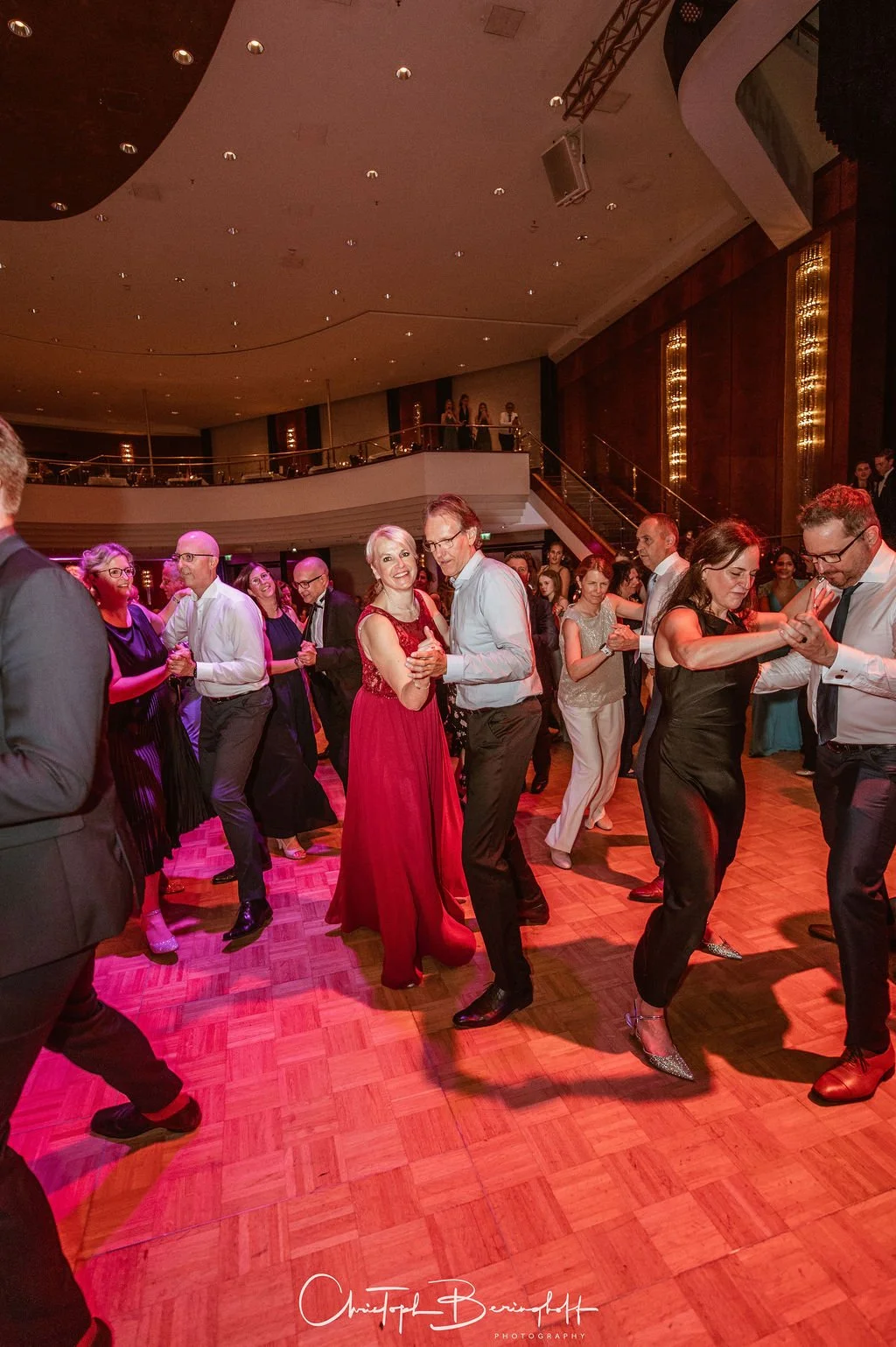 Menschen tanzen bei einer Party oder einem Ball in einem eleganten Veranstaltungsraum, viele in formeller Kleidung.