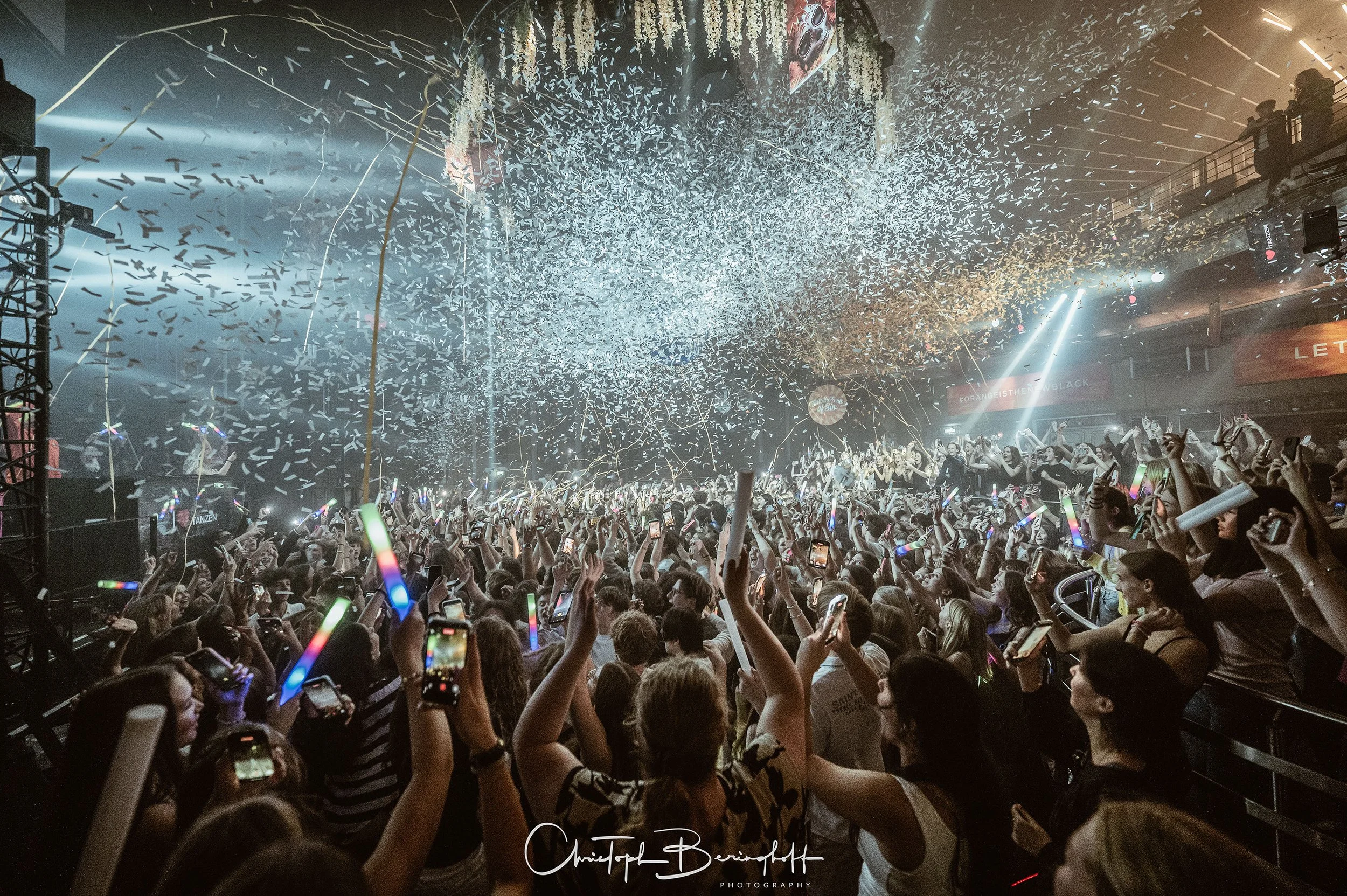 Menschenmenge bei einer Party im Club mit Konfetti, Lichtshows und Handyaufnahmen