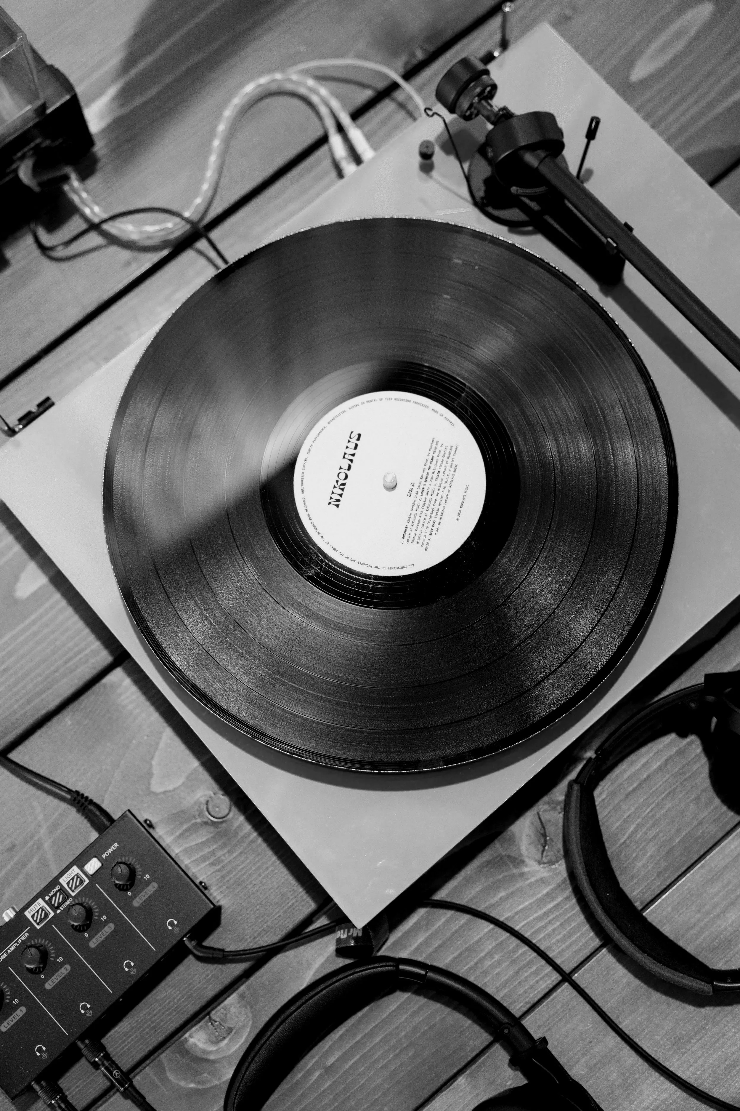 A gramophone record player playing a vinyl record, connected to a small audio mixer, with some wires on a wooden surface.