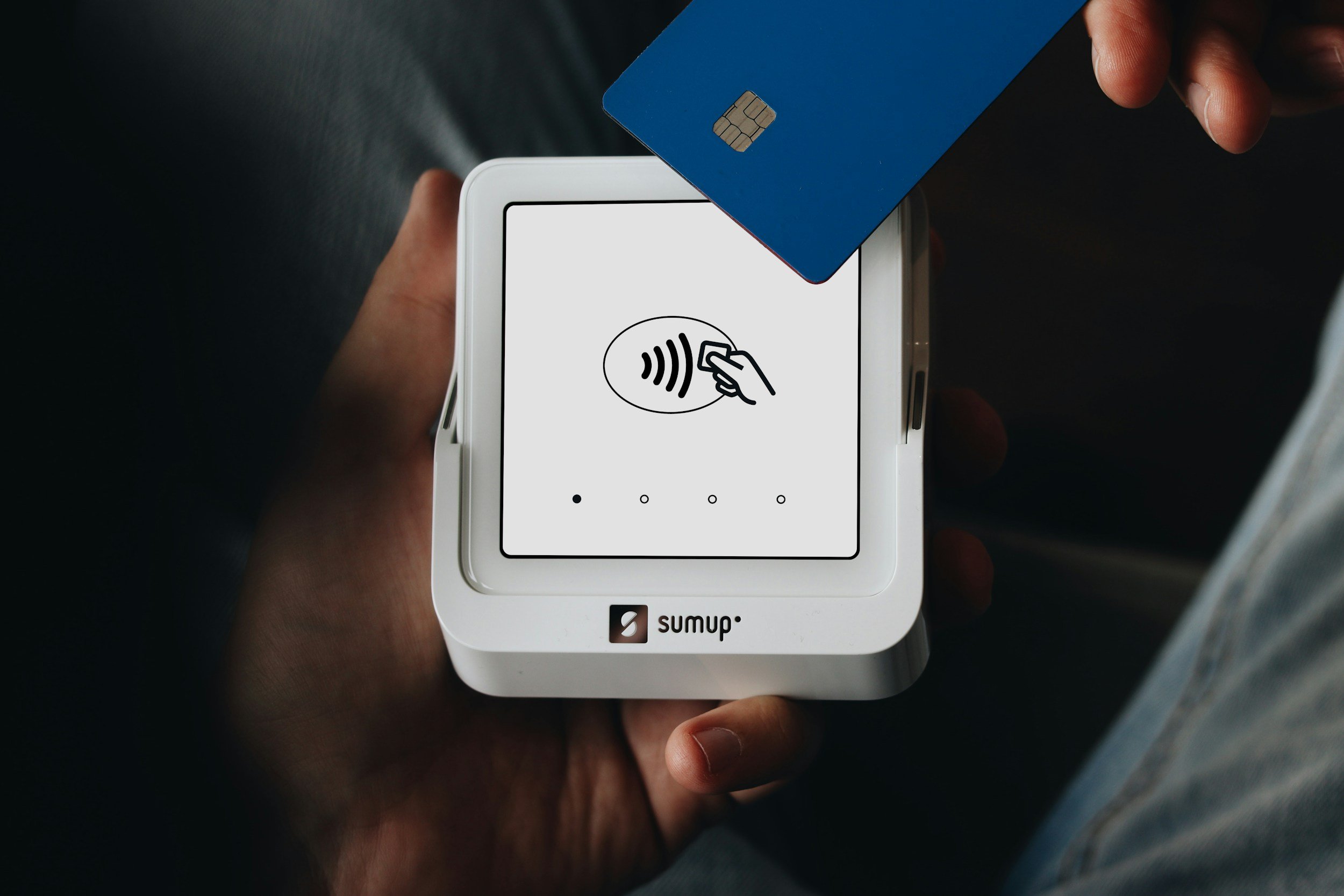 Person holding a contactless payment terminal and a blue credit card.